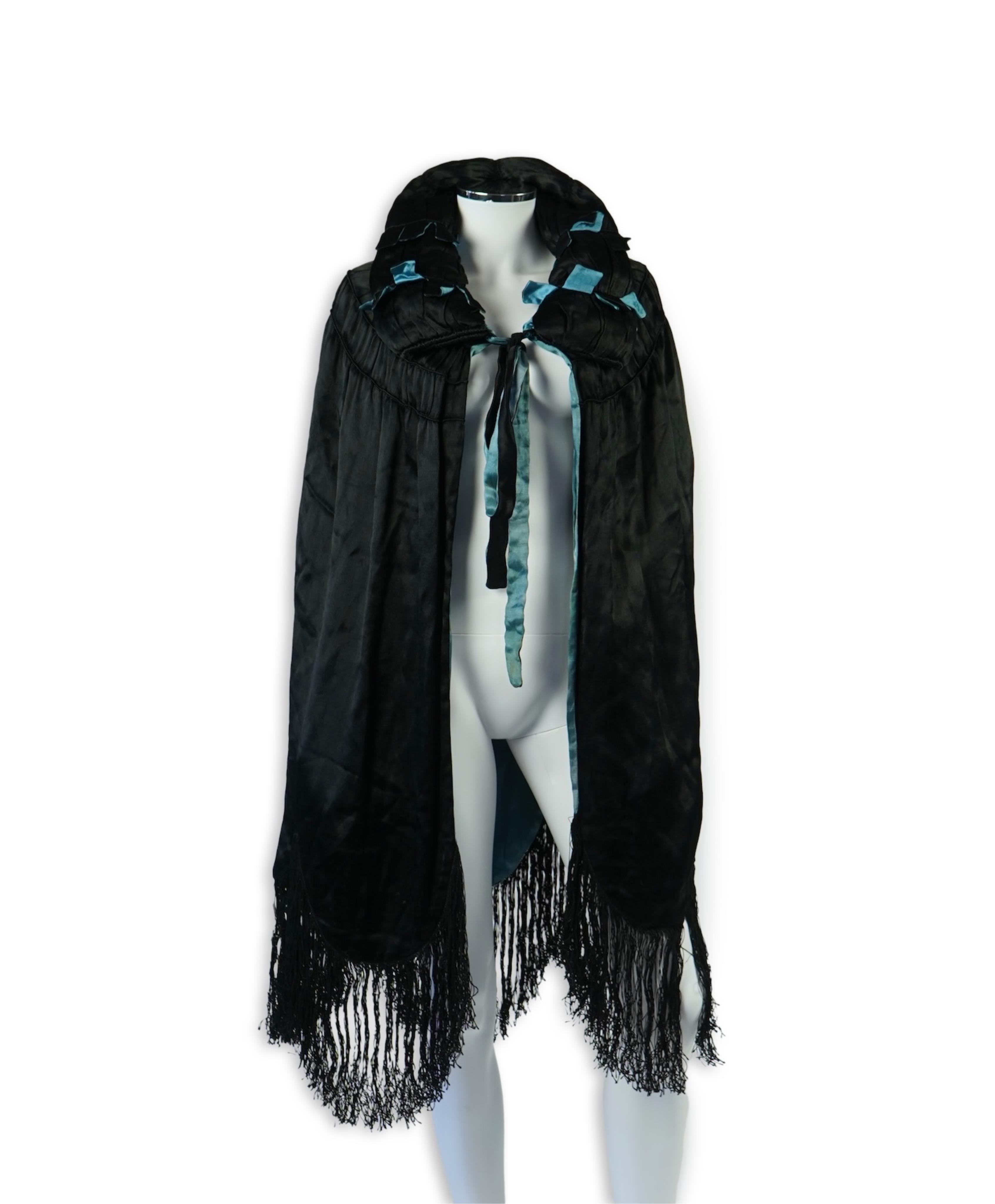 A 1920's ladies blue lined, black silk opera cape. Designed with a rushed ornate collar and scalloped and fringed lower edge. 95cm long fron neck to base. Condition - stained near the front edge, possibly removable with